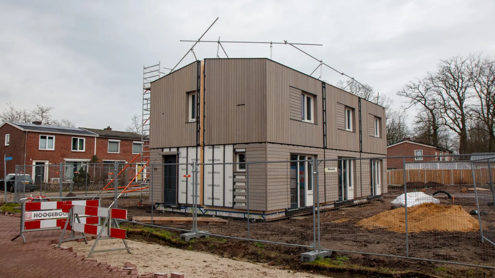 Moderne nieuwbouwwoning in aanbouw, omringd door steigers en bouwhekken