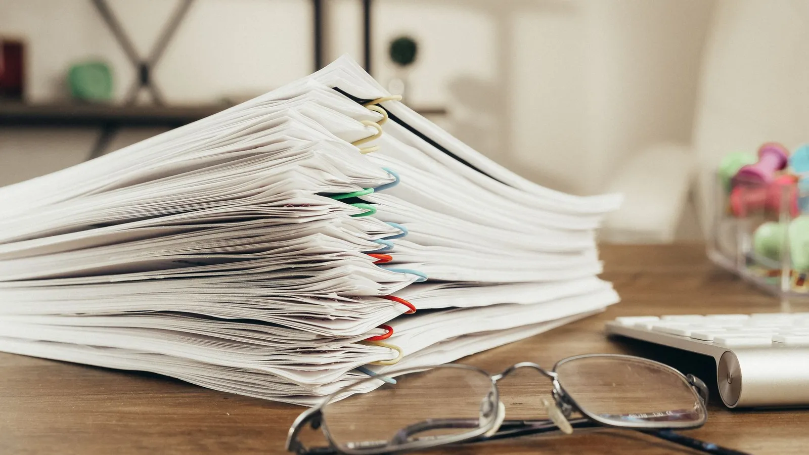 Stapel papieren documenten met een leesbril op een bureau
